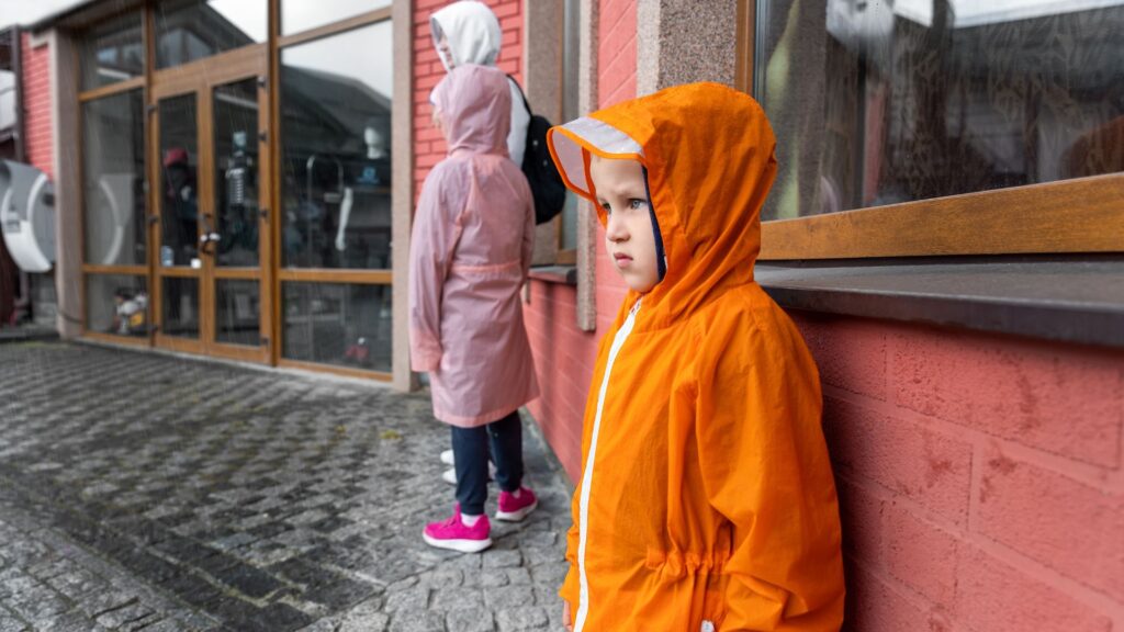 Chłopiec w pomarańczowym płaszczu, który schronił się przed deszczem